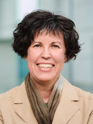Portrait von Diana Franke im sandfarbenen Mantel vor Glasfassade