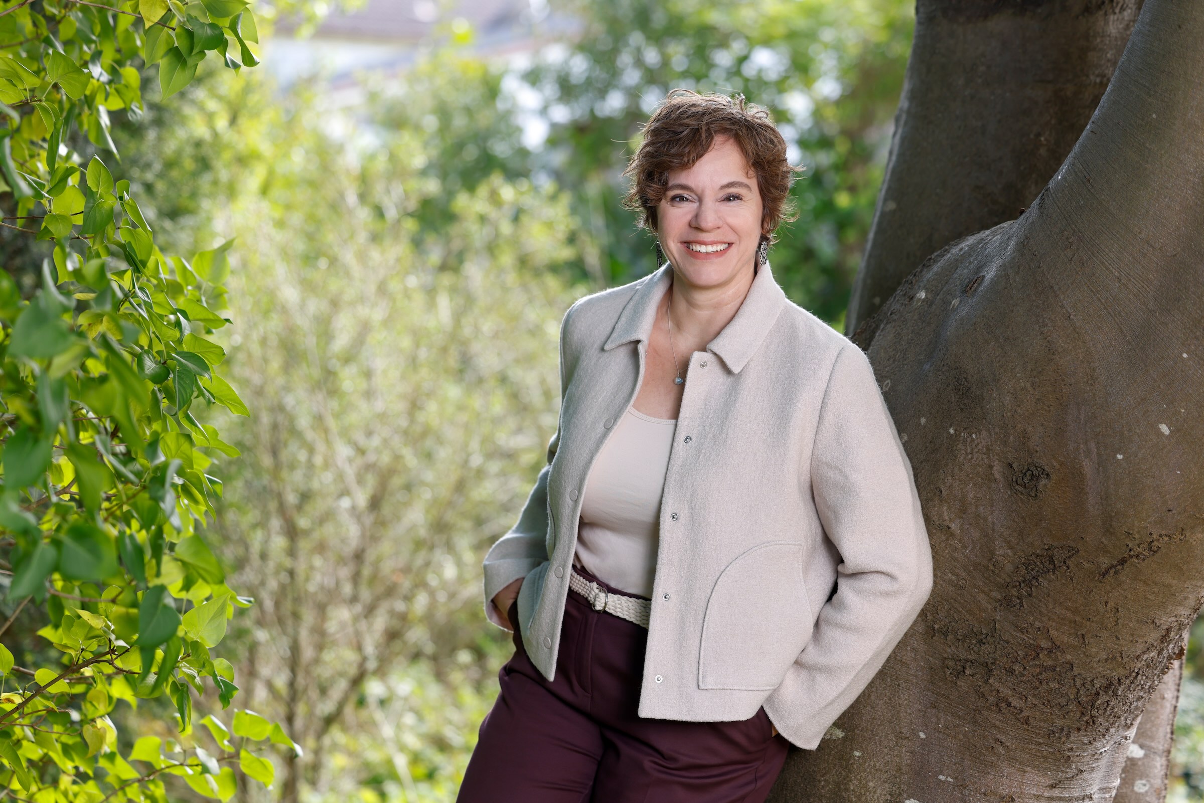 Melanie Kude im Wald stehend an Baum lehnend.